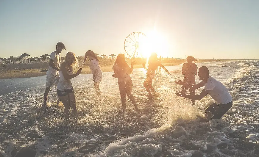 A group of people enjoying a beach at sunset, splashing in the water.