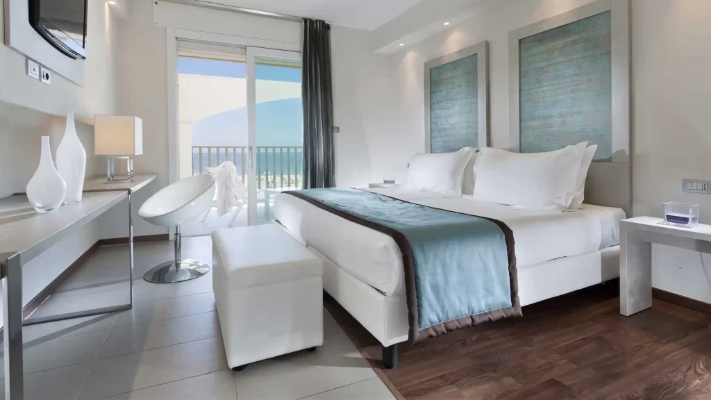 Camera d'albergo moderna e luminosa con letto matrimoniale e vista sul balcone.