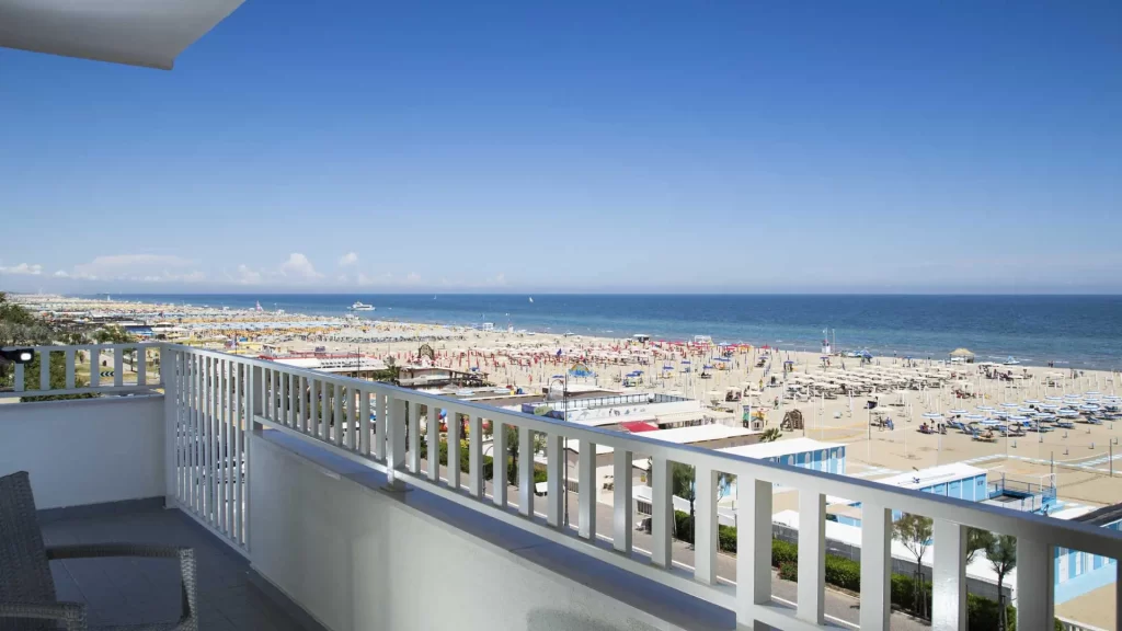 Balcone con vista su una spiaggia affollata e mare azzurro sotto un cielo limpido.
