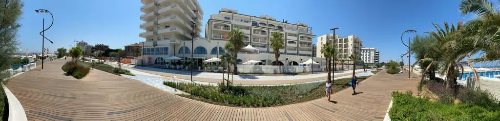 Vista panoramica di un lungomare con edifici e una passerella in legno.