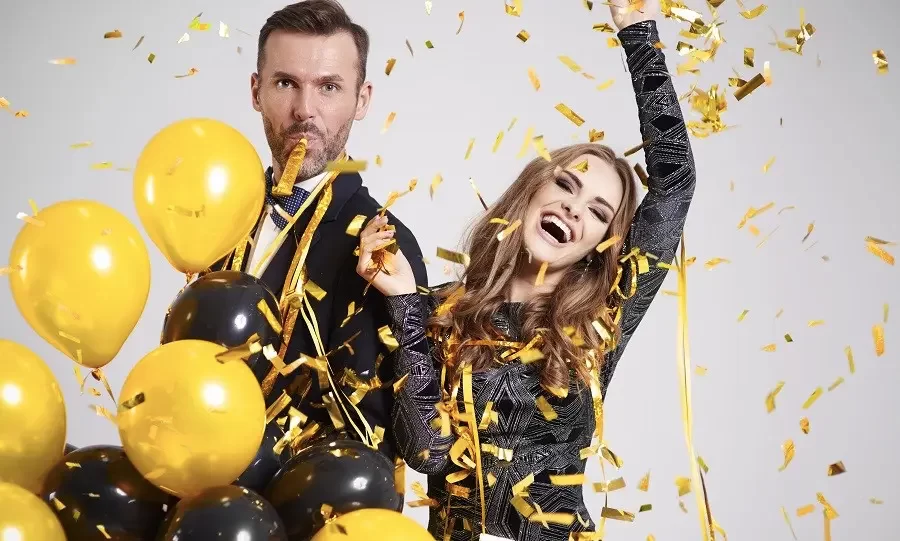 A joyful couple celebrating with black and yellow balloons and confetti.