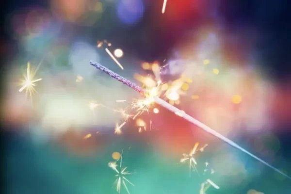 A sparkling lit sparkler with colorful bokeh lights in the background.