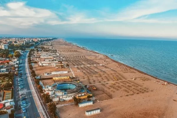 Aerial view of a long sandy beach with adjacent road and buildings along the coastline.