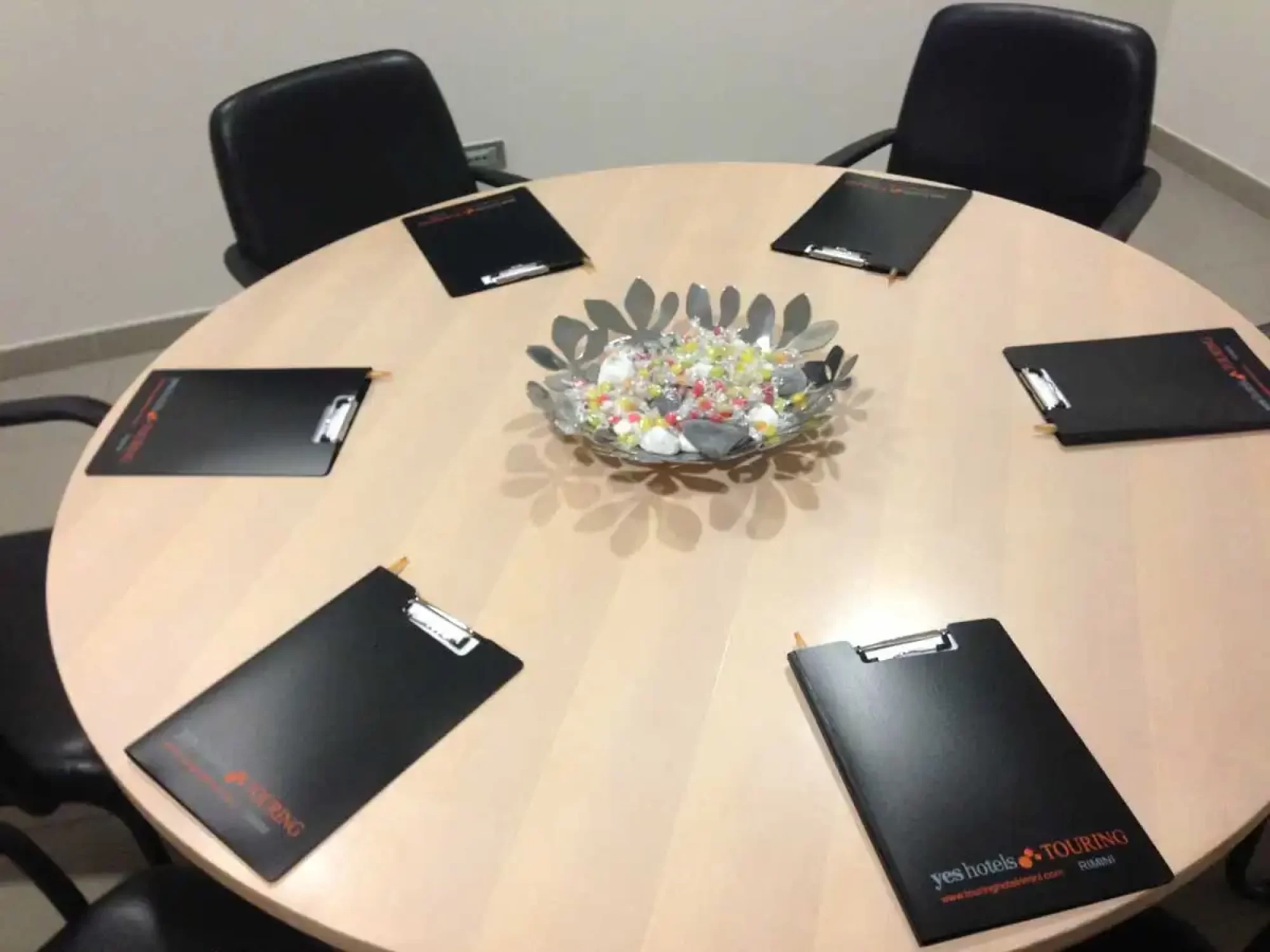 A round meeting table with clipboards and a bowl of candies.